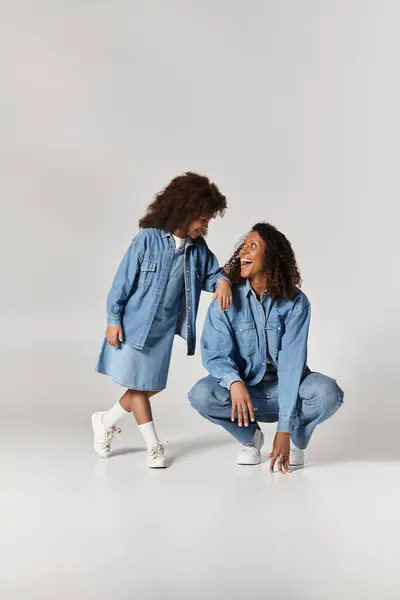 Afro-americano madre e figlia legame in corrispondenza denim abiti contro un pianura grigio sfondo. — Foto stock