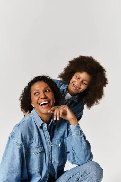 A happy African American mother and daughter wearing total denim outfits are laughing in the studio. — Stock Photo