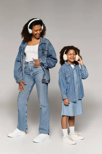 Stylish Black mom and daughter in matching denim, smiling with headphones. — Stock Photo