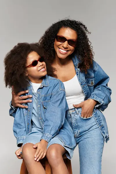 A stylish african american mother and daughter pose in matching denim outfits in a studio. — Stock Photo