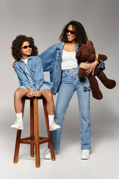 Black mother and daughter in matching denim outfits, grey background. — Stock Photo