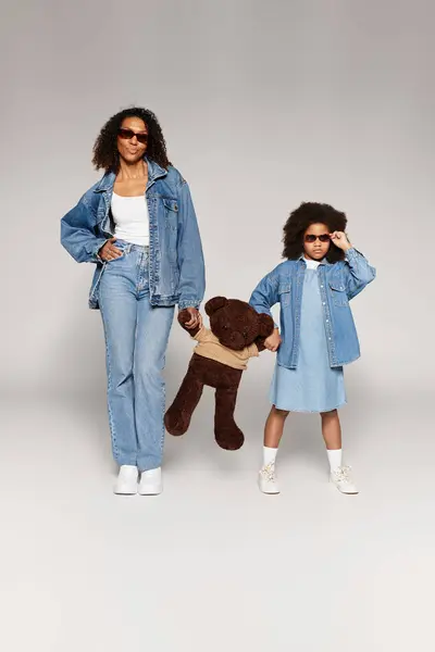 Madre e figlia afroamericana indossano entrambi abiti in denim in uno studio con uno sfondo grigio. — Foto stock