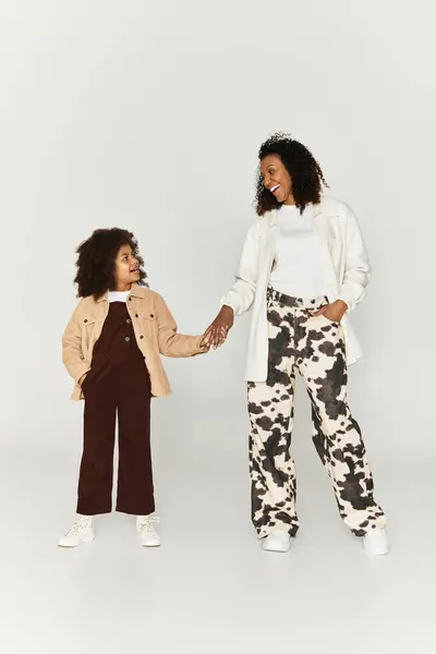 A mother and daughter joyfully hold hands, showcasing their trendy outfits against a soft backdrop. — Stock Photo