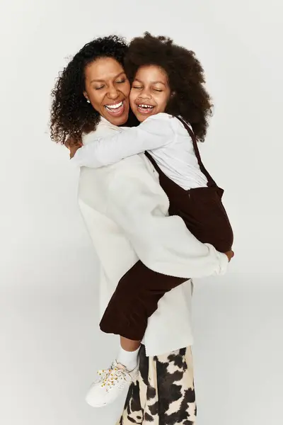 A mother holds her laughing daughter in a trendy studio setting, showcasing modern fashion. — Stock Photo