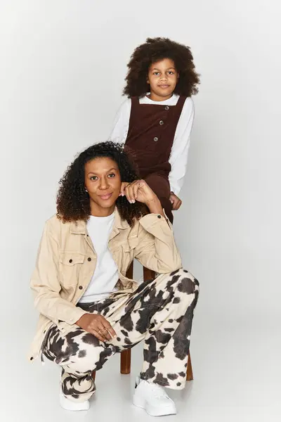 Élégante mère afro-américaine et sa fille posent dans des tenues tendances assorties dans un studio gris. — Photo de stock