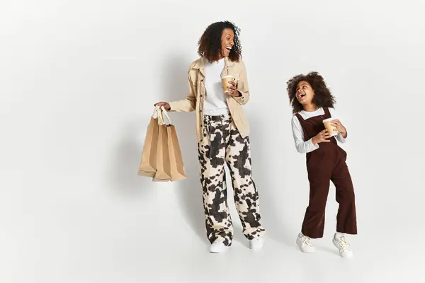 Mãe e filha na moda desfrutar de tempo juntos em roupas elegantes enquanto segurando bebidas. — Fotografia de Stock