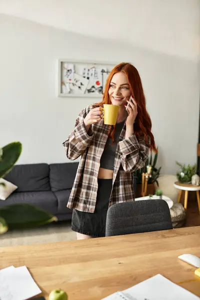 Bella giovane donna in abito casual si rilassa a casa, chiacchierando sul suo telefono e sorseggiando tè. — Foto stock