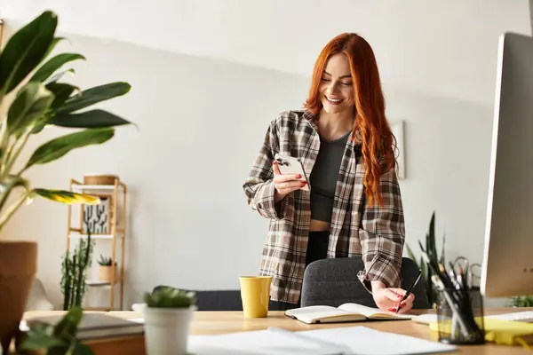 A beautiful young woman smiles as she looks at her phone, surrounded by a vibrant workspace. — Stock Photo