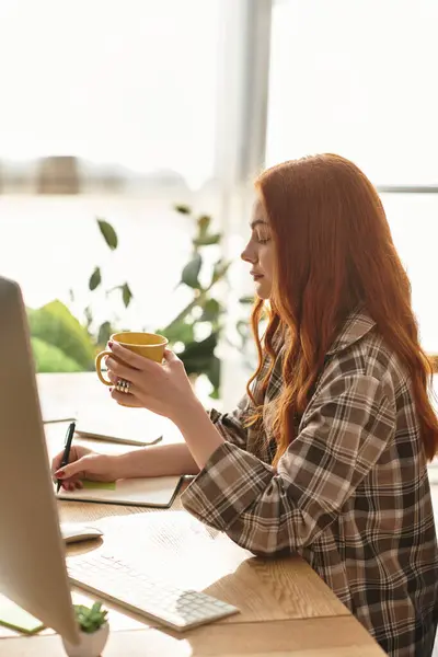 Young beautiful woman enjoys a warm beverage while writing in a comfortable setting. — Stock Photo