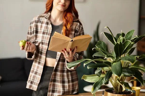 A young beautiful woman relaxes in a modern living room, reading a book while holding an apple. — Stock Photo
