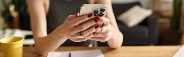 A young beautiful woman engages with her smartphone, sipping coffee in her cozy living space. — Stock Photo
