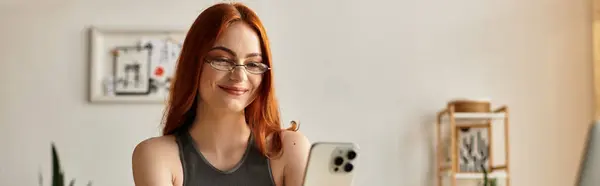 A young and beautiful woman smiles while browsing her phone in a warm and inviting room. — Stock Photo