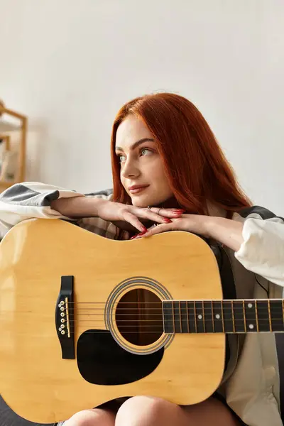 A young beautiful woman sits introspectively, holding a guitar, radiating creativity and calm. — Stock Photo