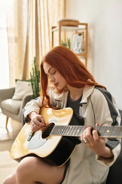 A young beautiful woman plays her guitar, immersed in her music, in a sunlit living room. — Stock Photo