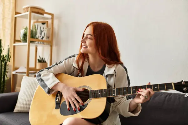 A young beautiful woman strums her guitar with a smile in a relaxed indoor environment. — Stock Photo