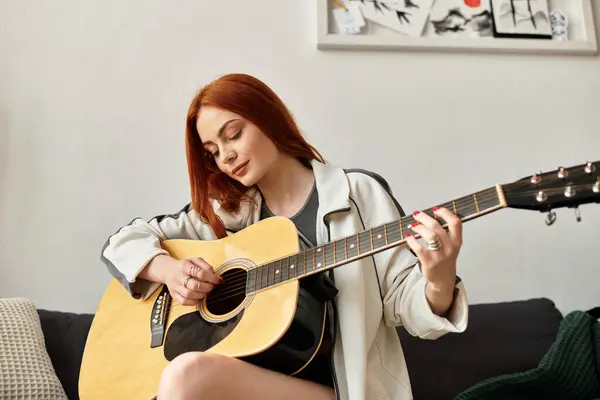 A young beautiful woman enjoys her spare time playing an acoustic guitar in her comfortable home. — Stock Photo