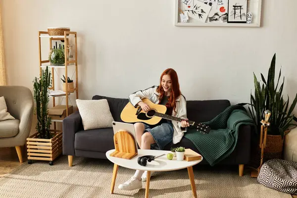 Joyeux jeune femme joue de la guitare sur un canapé confortable dans son élégant salon. — Photo de stock
