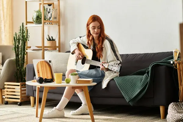 Una bella giovane donna suona la chitarra su un comodo divano nel suo elegante soggiorno. — Foto stock