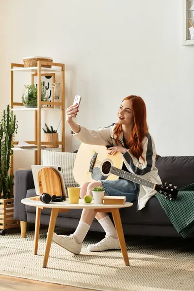 Young woman takes a selfie while playing guitar and relaxing in her cozy living room space. — Stock Photo