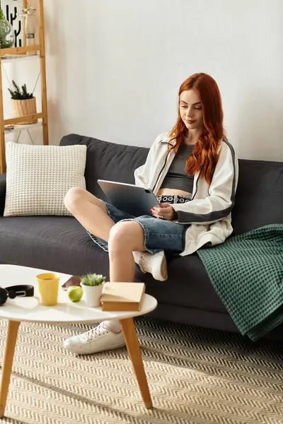 A young beautiful woman relaxes on a couch, working on her laptop while enjoying her spare time. — Stock Photo