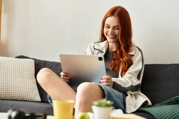 Una giovane donna sorride brillantemente mentre usa un tablet, godendo del suo tempo libero a casa. — Foto stock