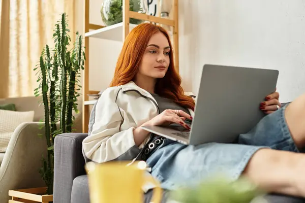 Bella donna si rilassa sul divano, focalizzata sul computer portatile in ambiente domestico invitante. — Foto stock