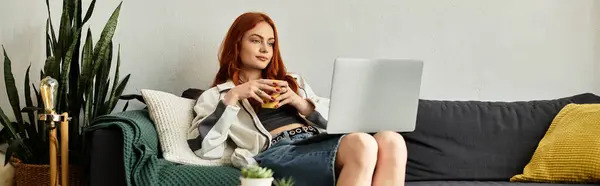 Una giovane bella donna siede su un accogliente divano, sorseggiando una bevanda calda e godendo il suo tempo libero. — Foto stock