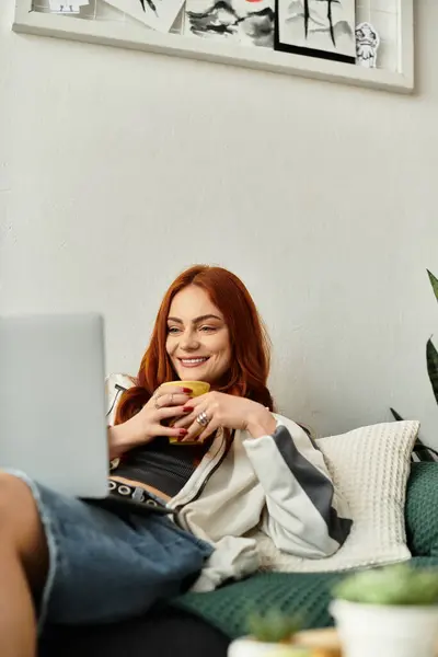Una giovane donna si rilassa su un divano, sorridendo mentre si gode il suo drink. — Foto stock