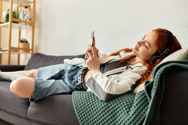 A young woman relaxes, enjoying music and browsing on her phone. — Stock Photo