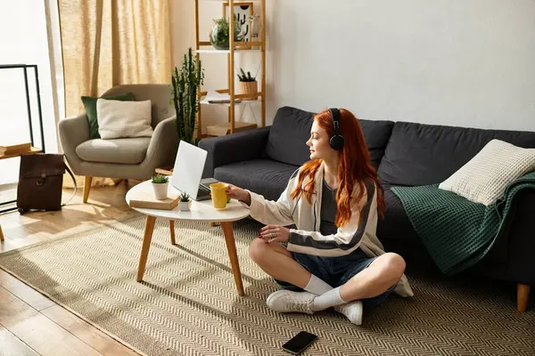 Junge Frau sitzt im Schneidersitz und nippt an Tee, während sie Musik in einem hellen, stilvollen Raum hört. — Stockfoto