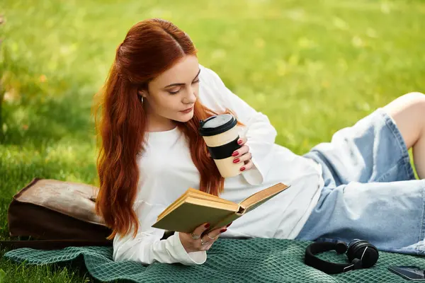 Молодая женщина расслабляется на траве, наслаждаясь книгой, потягивая кофе в теплый день. — стоковое фото