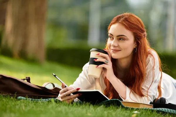 Relaxing outdoors, a young woman writes in her notebook while sipping coffee, smiling. — Stock Photo