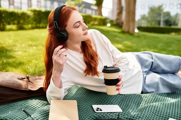 Una giovane bella donna si rilassa su una coperta verde, godendo il suo tempo libero con caffè e musica. — Foto stock