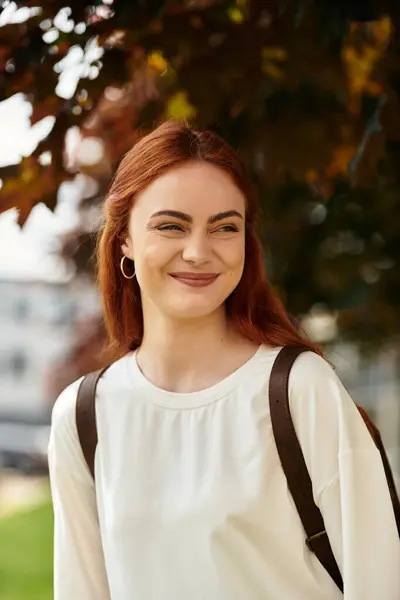A young beautiful woman stands outside, smiling joyfully amidst vibrant autumn foliage. — стоковое фото