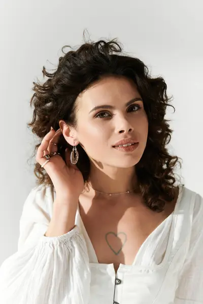 Une jeune femme confiante aux cheveux bouclés pose tout en ajustant ses boucles d'oreilles avec élégance. — Photo de stock