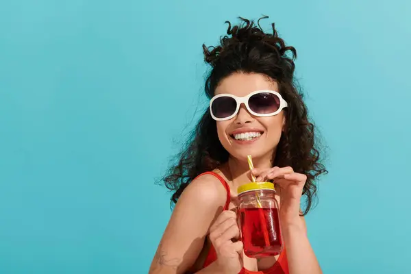 Eine junge Frau mit lockigem Haar und trendiger Sonnenbrille lächelt bei einem Drink. — Stockfoto