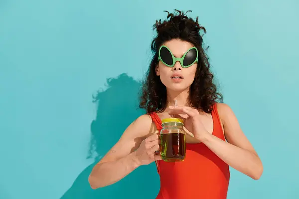 Sporting a bold swimsuit and quirky sunglasses, a young woman enjoys a refreshing drink. — Stock Photo
