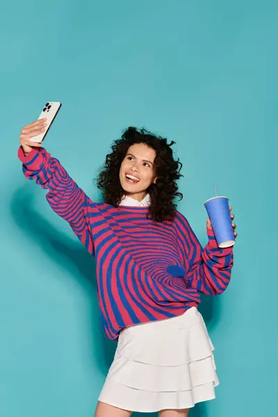 A joyful young woman snaps a selfie while enjoying a cool drink in a bright setting. — стоковое фото