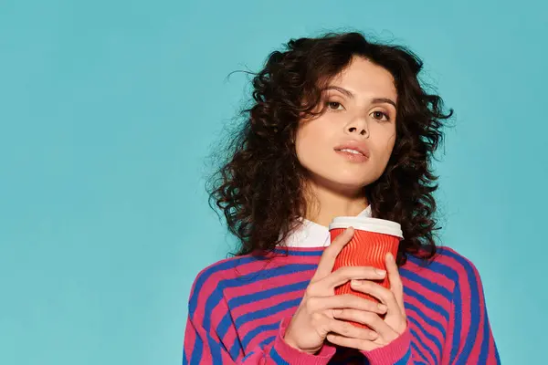 Una giovane donna sicura di sé con i capelli ricci beve caffè, vestita con abiti chic e colorati. — Foto stock
