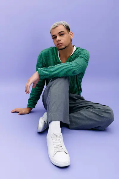 A young Black man with dyed hair poses confidently in a trendy outfit against a purple backdrop. — Stock Photo