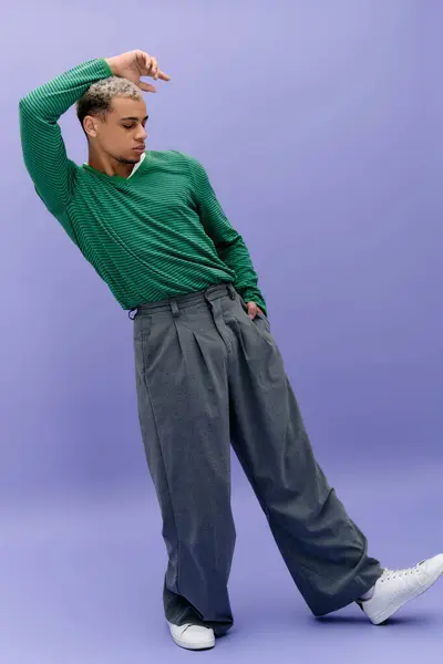 Un jeune homme aux cheveux teints pose en toute confiance dans une tenue à la mode sur un fond violet. — Photo de stock