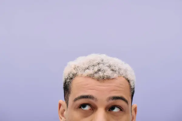 Un joven afroamericano con el pelo teñido mirando hacia otro lado sobre fondo púrpura - foto de stock