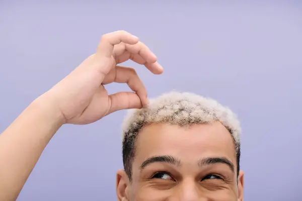 Un joven afroamericano con el pelo teñido muestra su peinado, sonriendo felizmente - foto de stock