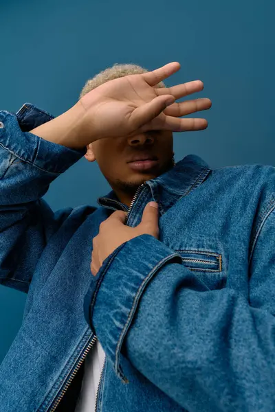 Un hombre negro joven con estilo en una chaqueta de mezclilla posa sobre un fondo vibrante. — Stock Photo