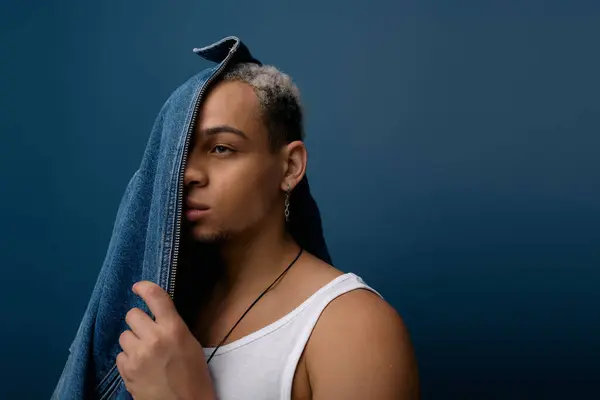 Un joven negro muestra su estilo en una chaqueta de mezclilla con un fondo azul. - foto de stock