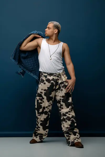 Un joven afroamericano confiado muestra una mirada de moda contra un telón de fondo azul. - foto de stock