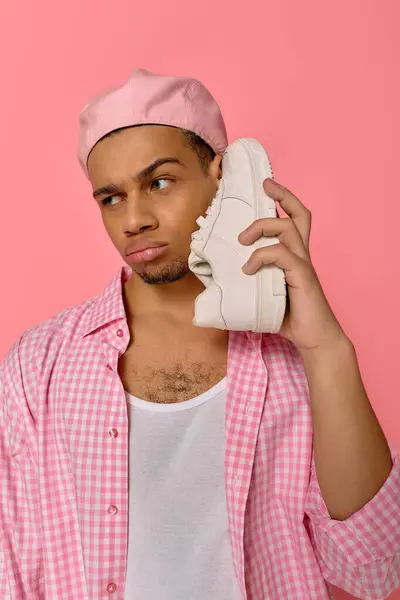 Un joven negro muestra su estilo con una boina y una camisa a cuadros, sosteniendo una zapatilla de deporte. - foto de stock