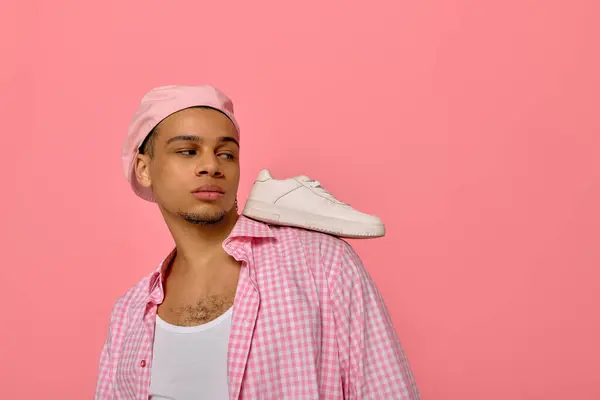 Un joven negro muestra su estilo con una boina elegante y una camisa a cuadros sobre un fondo rosa. - foto de stock
