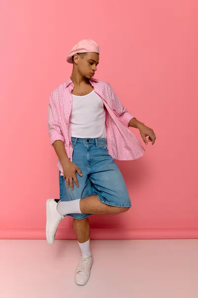 Un jeune homme noir élégant pose en toute confiance sur un fond rose vif dans un béret chic et chemise. — Photo de stock