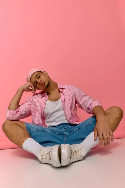 A confident young man showcases his fashion sense in a checkered shirt and beret on a pink backdrop. — Stock Photo